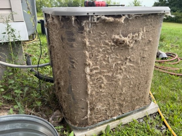 Outdoor AC condenser thickly clogged with cottonwood fluff and debris before cleaning