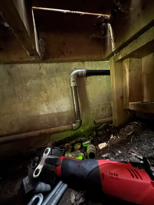New metal pipe elbows installed through a concrete foundation wall in a crawl space
