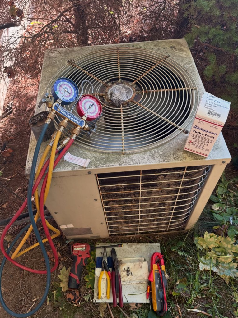 Outdoor condenser with manifold gauges, a capacitor, and hand tools on the ground