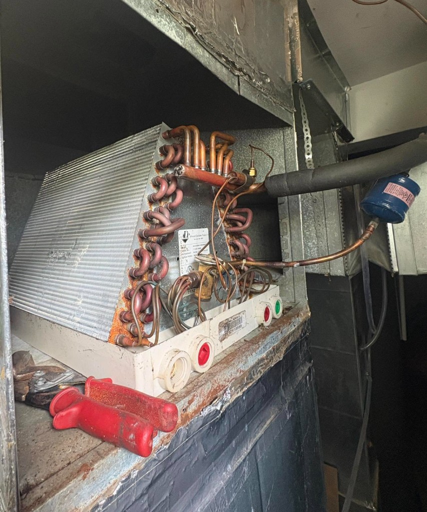 Evaporator coil opened inside a metal plenum, with copper lines and a filter-drier