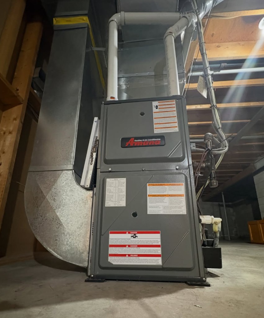 Gray Amana furnace connected to metal ductwork and a gas line in a mechanical room