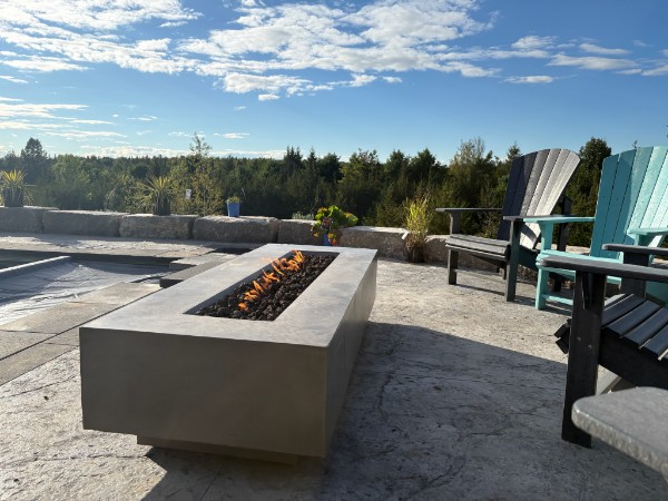 Rectangular gas fire pit burning on a stone patio beside a pool