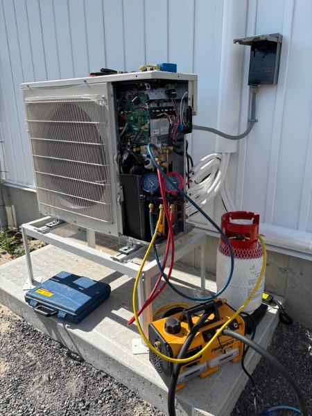 Outdoor heat pump with the side panel open, manifold gauges connected, and a vacuum pump on the pad