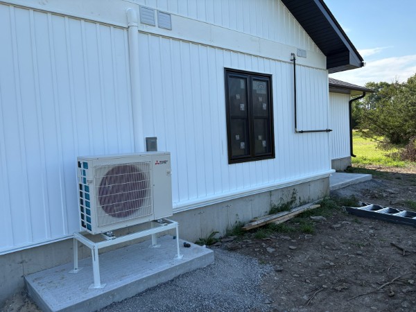 Mitsubishi Electric outdoor heat pump on a metal stand against white house siding