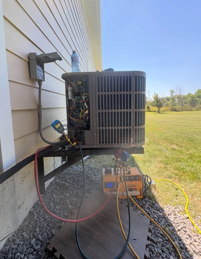 Outdoor air conditioner with the side panel off, gauges connected, and a recovery machine on the ground